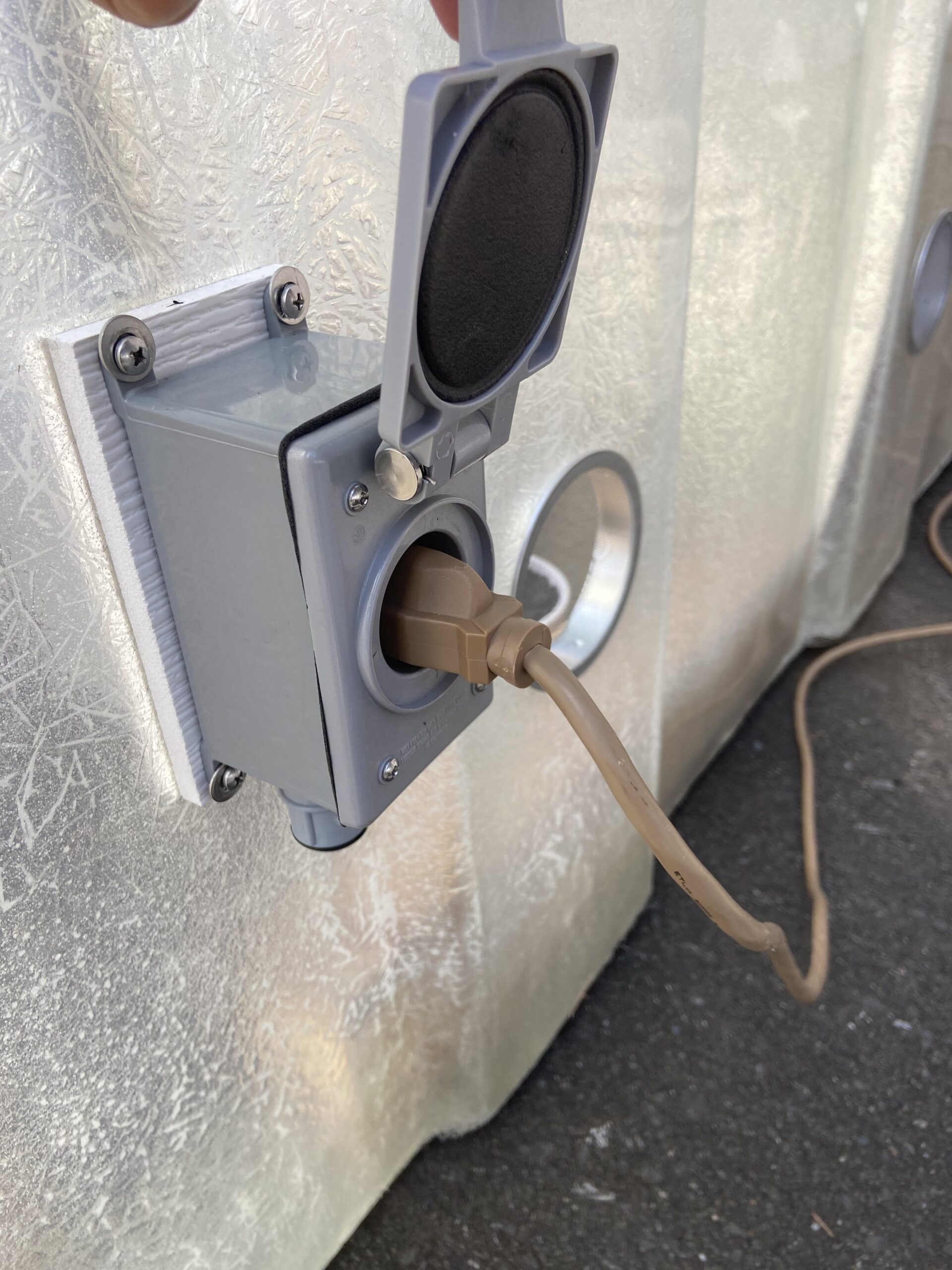 A brown power cord plugged into an Electrical Outlet Package with a lifted protective cover.