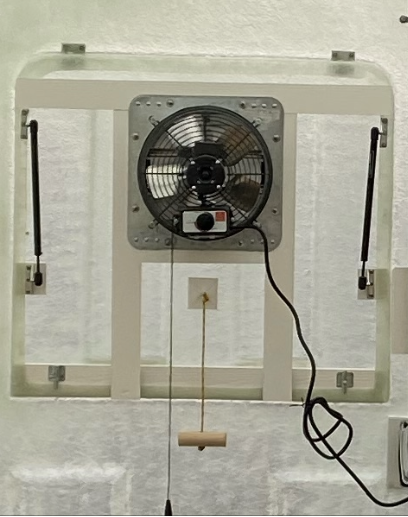 A Rear Window Fan featuring a square exhaust fan in a rectangular frame with two gas struts on a white surface.