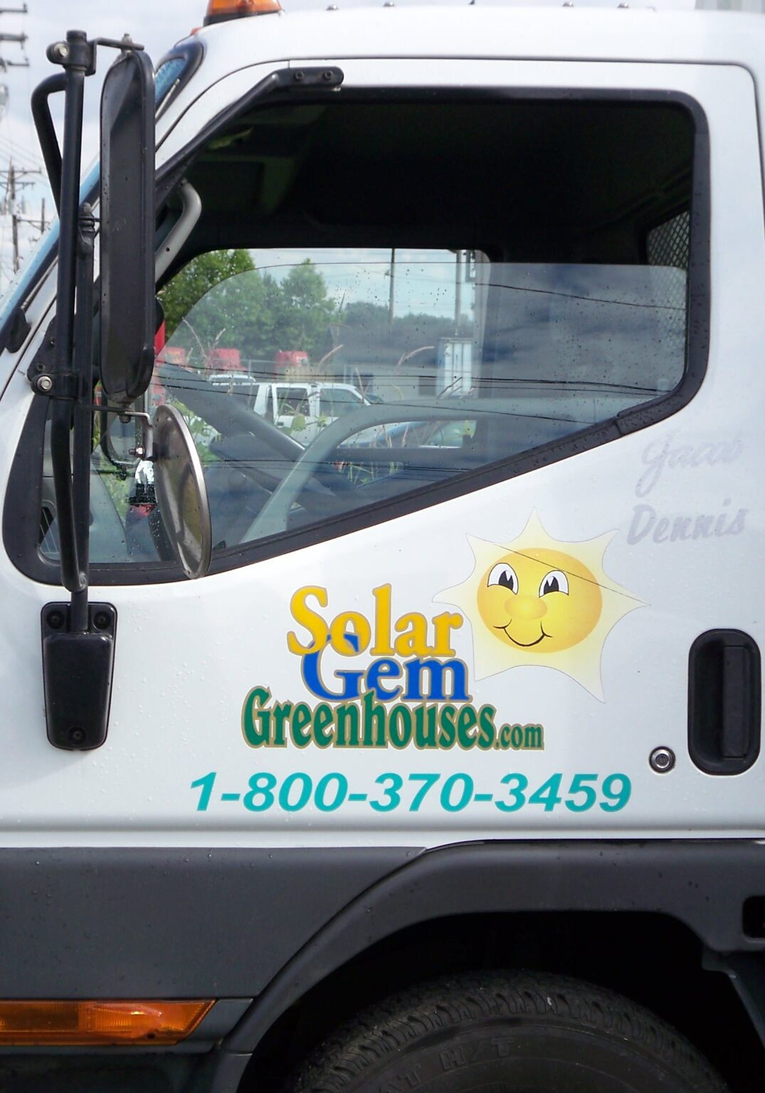 White truck with the Solar Gem Greenhouses logo, mascot, and phone number on the door.